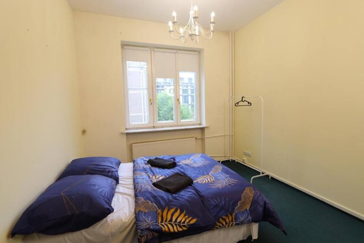 A bedroom with a bed, a window, a radiator, and a hanging light fixture.