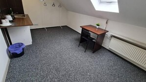 A small, compact room with a sloped ceiling, a skylight, a radiator, a desk with a chair, and a small plant. - Fantastic Inn Warsaw - NS42 (Warsaw)