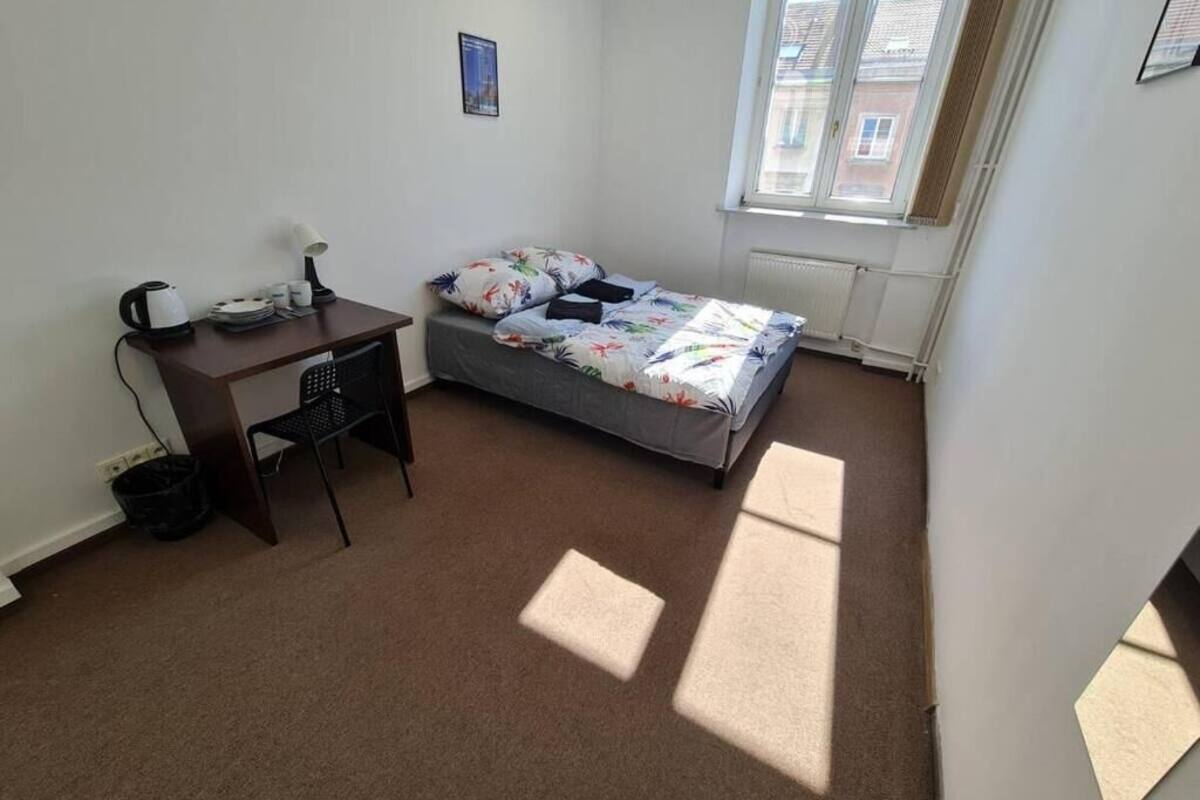 A small, well-lit bedroom with a single bed, a desk, and a chair.