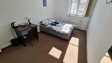 Un dormitorio pequeño y bien iluminado con una cama individual, un escritorio y una silla.