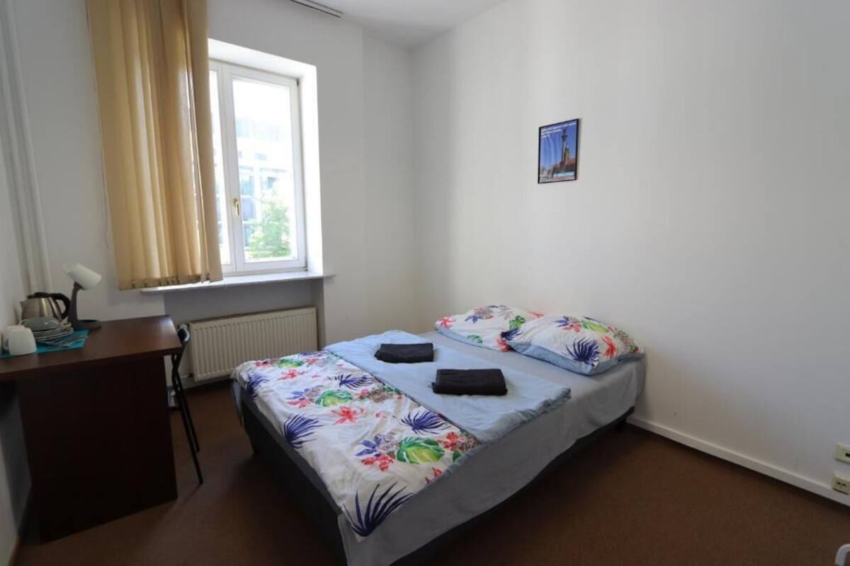 A small, tidy bedroom with a bed, a desk, and a window with curtains.