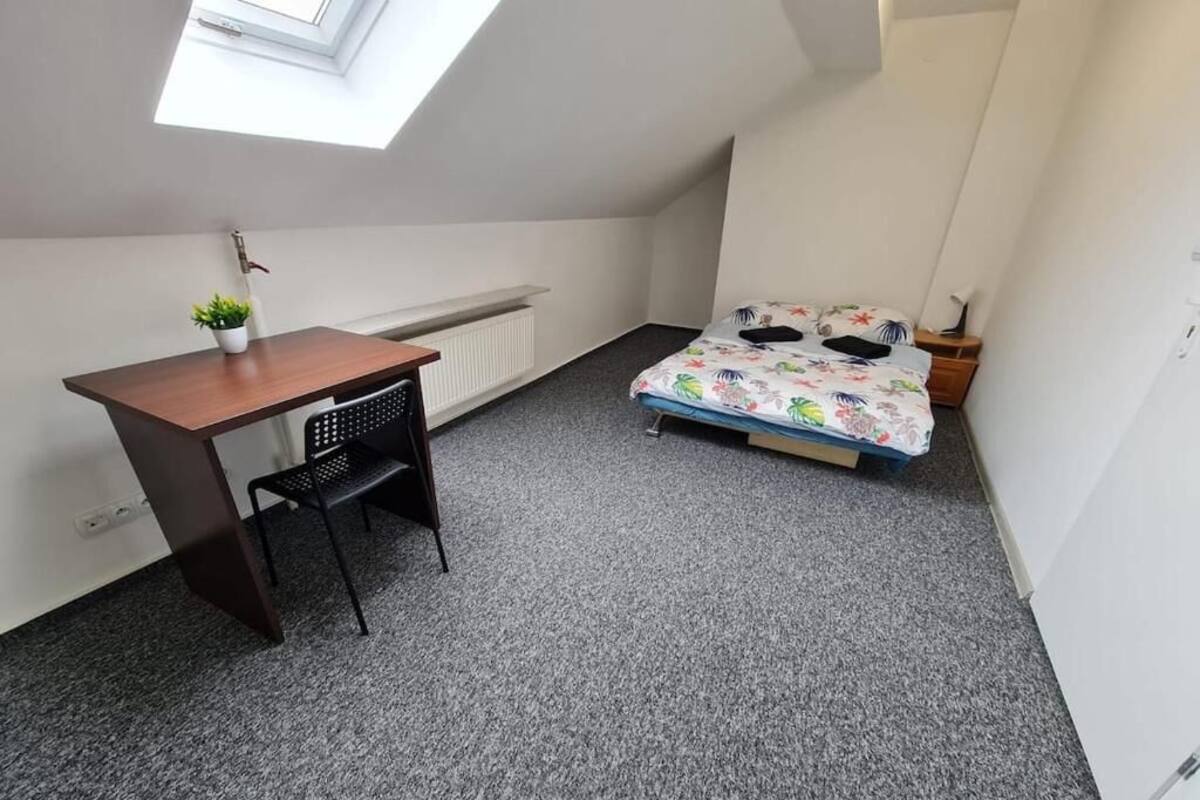 A small, well-lit room with a skylight, a bed with floral bedding, a desk with a chair, and a radiator.