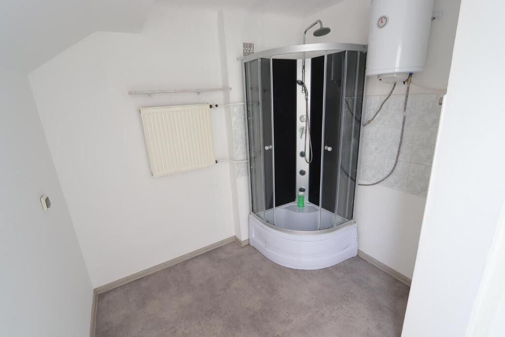 A corner bathroom with a glass-enclosed shower, a white radiator, and a white toilet.