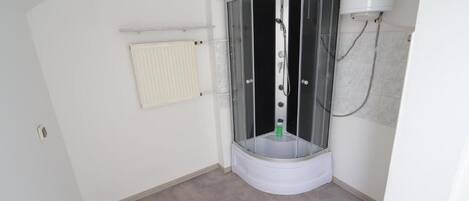 Ein Badezimmer im Eckbereich mit einer gläsernen Duschkabine, einem weißen Heizkörper und einer weißen Toilette.