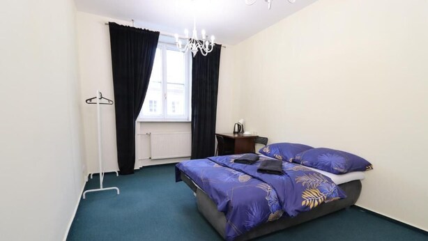 Une chambre à coucher comprenant un lit, un radiateur, une fenêtre avec des rideaux, un luminaire suspendu et un porte-manteau.