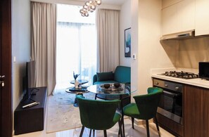 A modern kitchen with a gas stove, a dining area with a glass table and chairs, and a sofa in the background.