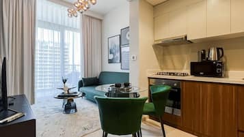 Un soggiorno moderno con un divano verde, un tavolino da caffè e una TV. È presente un angolo cottura con fornelli, microonde e pensili.