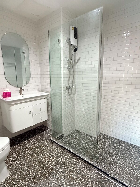 A modern bathroom with a glass-enclosed shower, white subway tiles, a white vanity with drawers, and a round mirror. - Luck Hotel Huai Khwang MRT Ratchada (Bangkok)