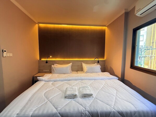 Habitación de hotel con una cama grande, dos mesitas de noche, una lámpara de pared y una ventana con vistas al exterior.