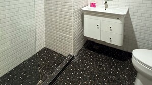 A bathroom with white subway tile walls, a white sink with a mirror, and a black speckled floor. - Luck Hotel Huai Khwang MRT Ratchada (Bangkok)