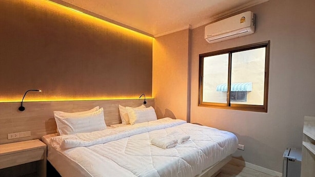 A modern bedroom with a large bed, bedside tables, an air conditioning unit, and a window with a view. - Luck Hotel Huai Khwang MRT Ratchada (Bangkok)