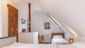 A bedroom with two beds, a radiator, a desk, and a ceiling light. - "Strandläufer" apartment: Charming maisonette impresses with its spacious living and (Harlesiel)
