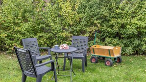 A garden with two chairs and a table, a small wooden cart, and a hedge in the background. - "Strandläufer" apartment: Charming maisonette impresses with its spacious living and (Harlesiel)