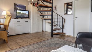 A modern living room with a spiral staircase, a television, a sofa, and a dining table. - "Strandläufer" apartment: Charming maisonette impresses with its spacious living and (Harlesiel)