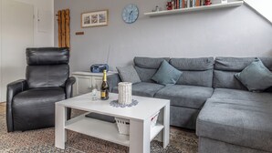 A living room with a grey sofa, a black leather chair, a white coffee table, and a bookshelf with books and decorative items. - "Strandläufer" apartment: Charming maisonette impresses with its spacious living and (Harlesiel)