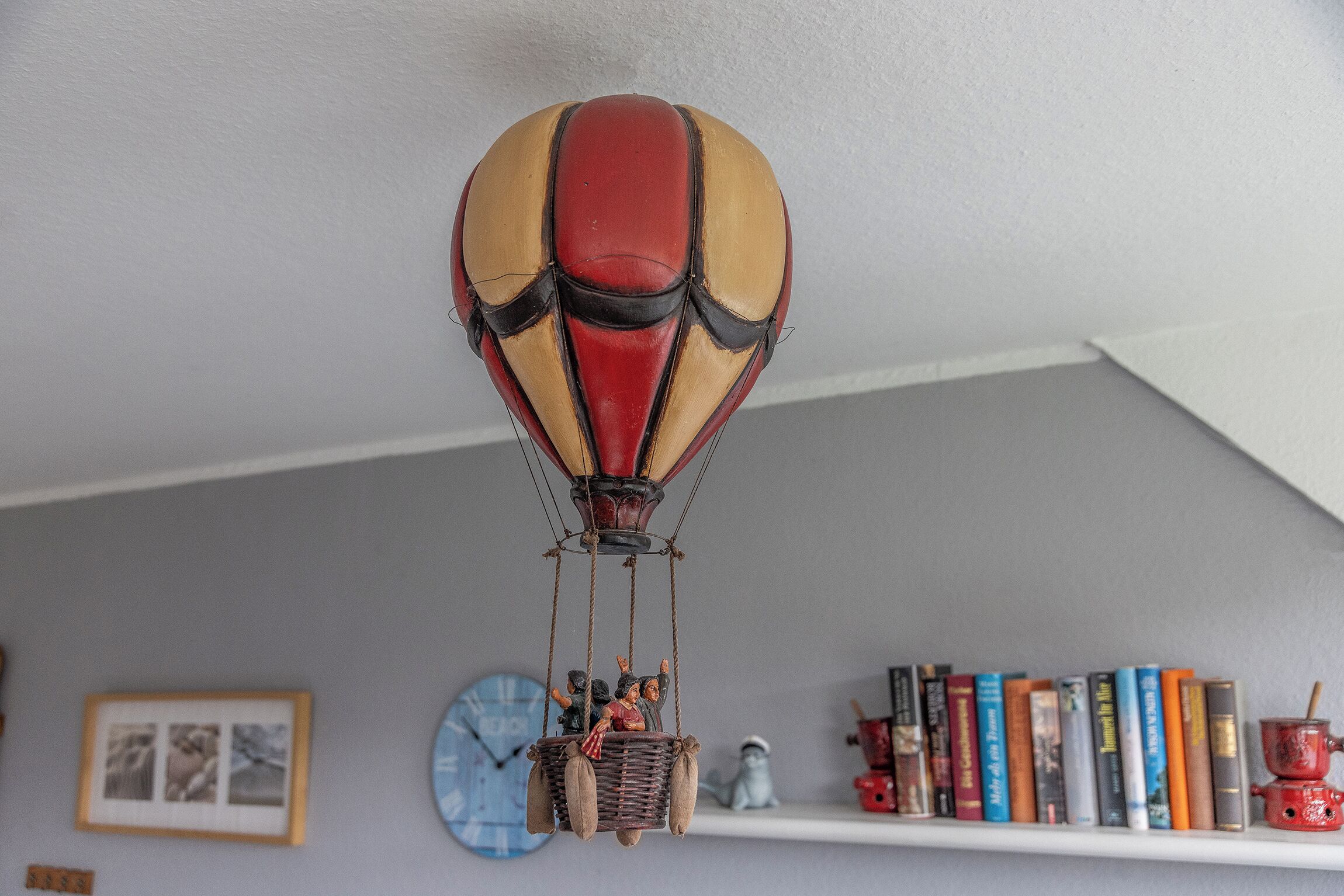 Un globo aerostático decorativo colgando del techo, un reloj y una estantería con libros y adornos.