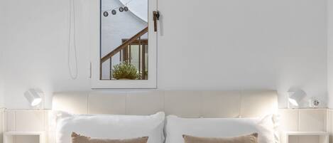 Un dormitorio con cama, dos almohadas, mesitas de noche, una ventana y vistas al exterior.