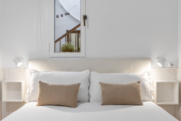 A bedroom with a bed, two pillows, bedside tables, a window, and a view of the outside.