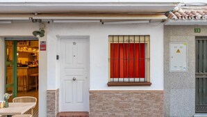 A white door with the number 19, a window with red curtains, a small outdoor seating area with wicker chairs, and a tiled floor. - Holiday Home 'Casa Marbella' with Private Terrace, Wi-Fi and Air Conditioning (Fuengirola)