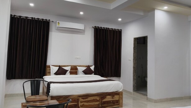 A modern bedroom with a wooden bed frame, a small wooden table, and two chairs. - Hotel Yaduraj By Salasar Hospitality (Udaipur)