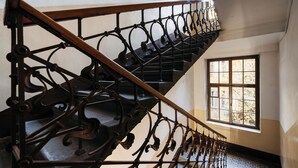 Una scala con ringhiere in metallo decorate e corrimano in legno, che conduce a una stanza con una grande finestra.