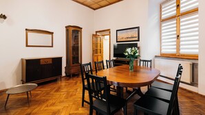 Un'area pranzo con un tavolo di legno, sedie nere, un armadietto, una televisione e una finestra con persiane.