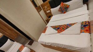 Une chambre d’hôtel avec deux lits, chacun doté d’un cadre en bois et de draps blancs. On y trouve une table de chevet en bois, sur laquelle sont posés une lampe et un téléphone.