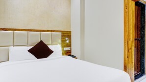 Un lit bien fait, avec une tête de lit en bois, un téléphone sur la table de chevet et une lampe fixée au mur.