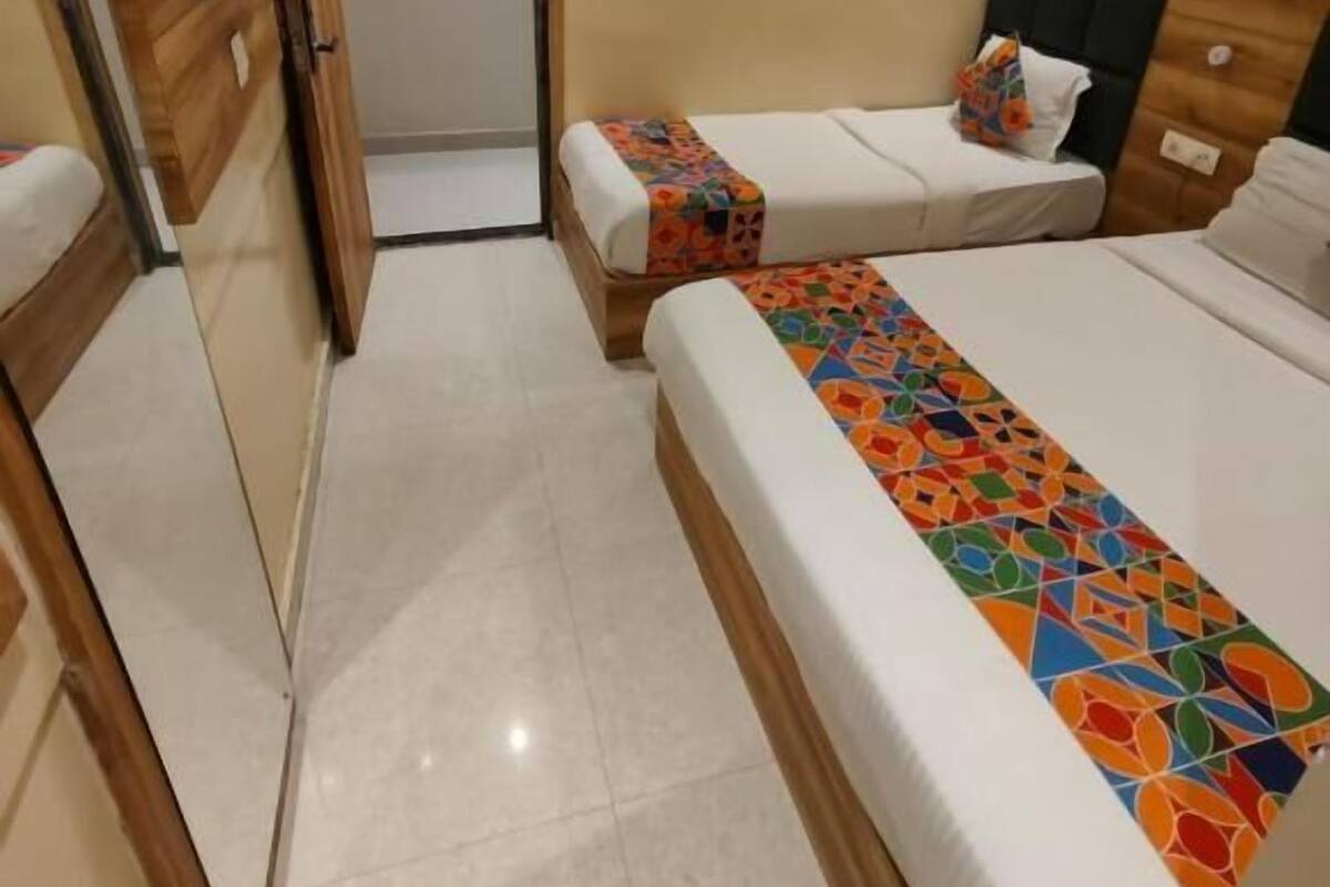 A hotel room with two single beds, a larger bed, a TV mounted on the wall, and a door leading to another room.