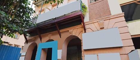A building with a blue door, arched windows, and a balcony with plants.