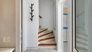 Un pasillo con una escalera, un perchero y una puerta que da a otra habitación.