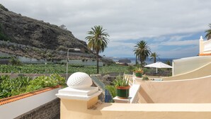 Una terraza en la azotea con vistas a un paisaje costero, palmeras y una escultura esférica blanca.