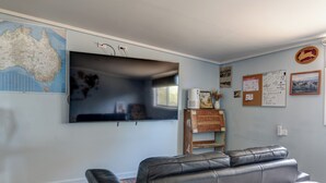 A room with a large flat-screen TV mounted on the wall, a leather sofa, a patterned rug, and a map of Australia.