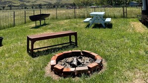 A grassy outdoor area with a fire pit, picnic table, and bench.