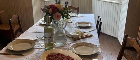 A dining table set for four with a central dish of food, wine glasses, and a vase of flowers.