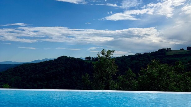 Une piscine d’eau cristalline, d’un bleu éclatant, avec vue sur une colline boisée et un ciel partiellement nuageux.
