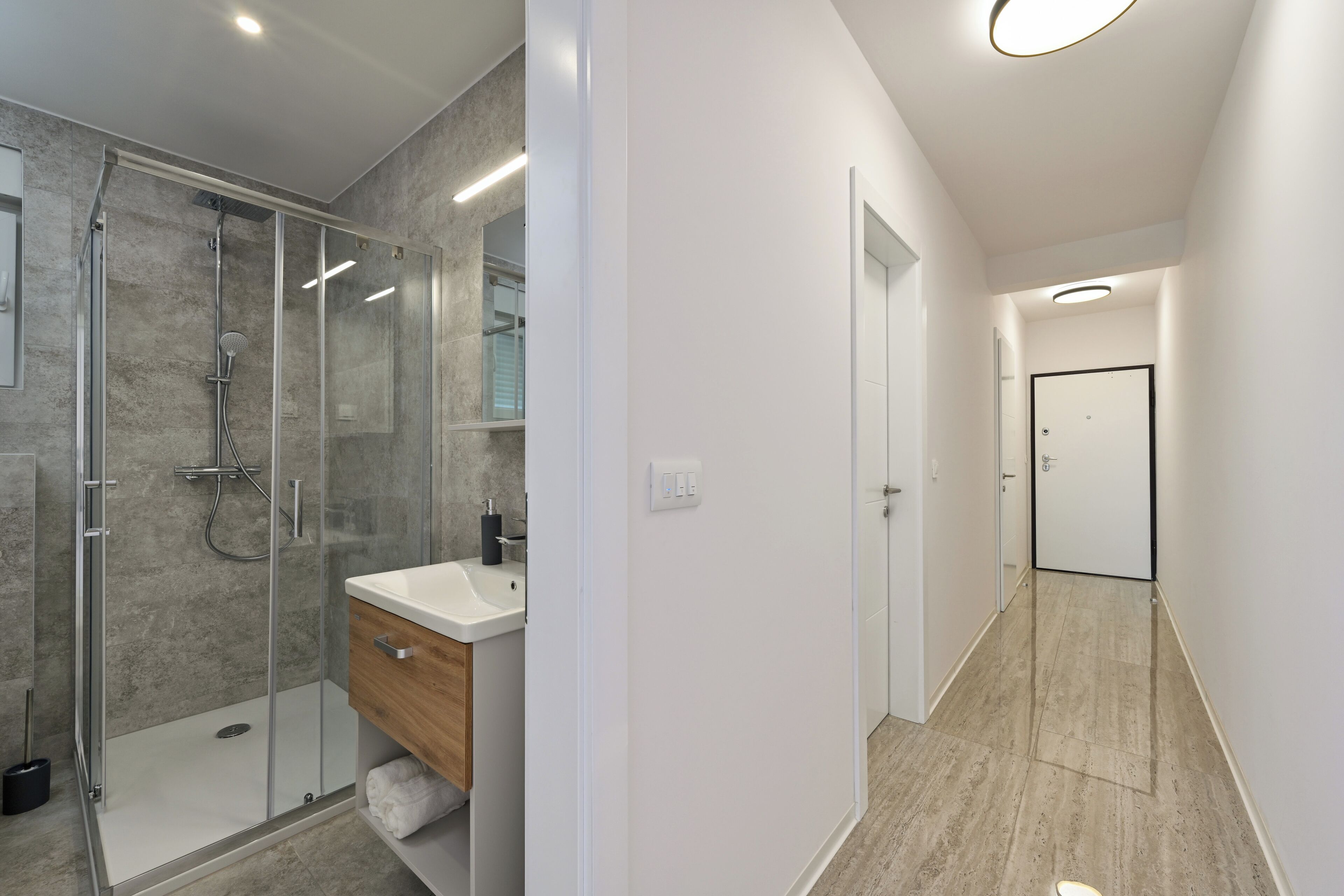 A modern bathroom with a glass-enclosed shower, a wooden vanity, and a white sink.