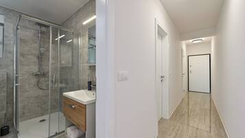 A modern bathroom with a glass-enclosed shower, a wooden vanity, and a white sink.