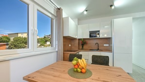 A modern kitchen with white cabinets, a microwave, and a sink. A wooden table with a fruit basket is in the foreground. - Apartment Amarilis (Kolan)