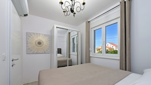 A bedroom with a large bed, a chandelier, a window with curtains, and a mirror. - Apartment Amarilis (Kolan)