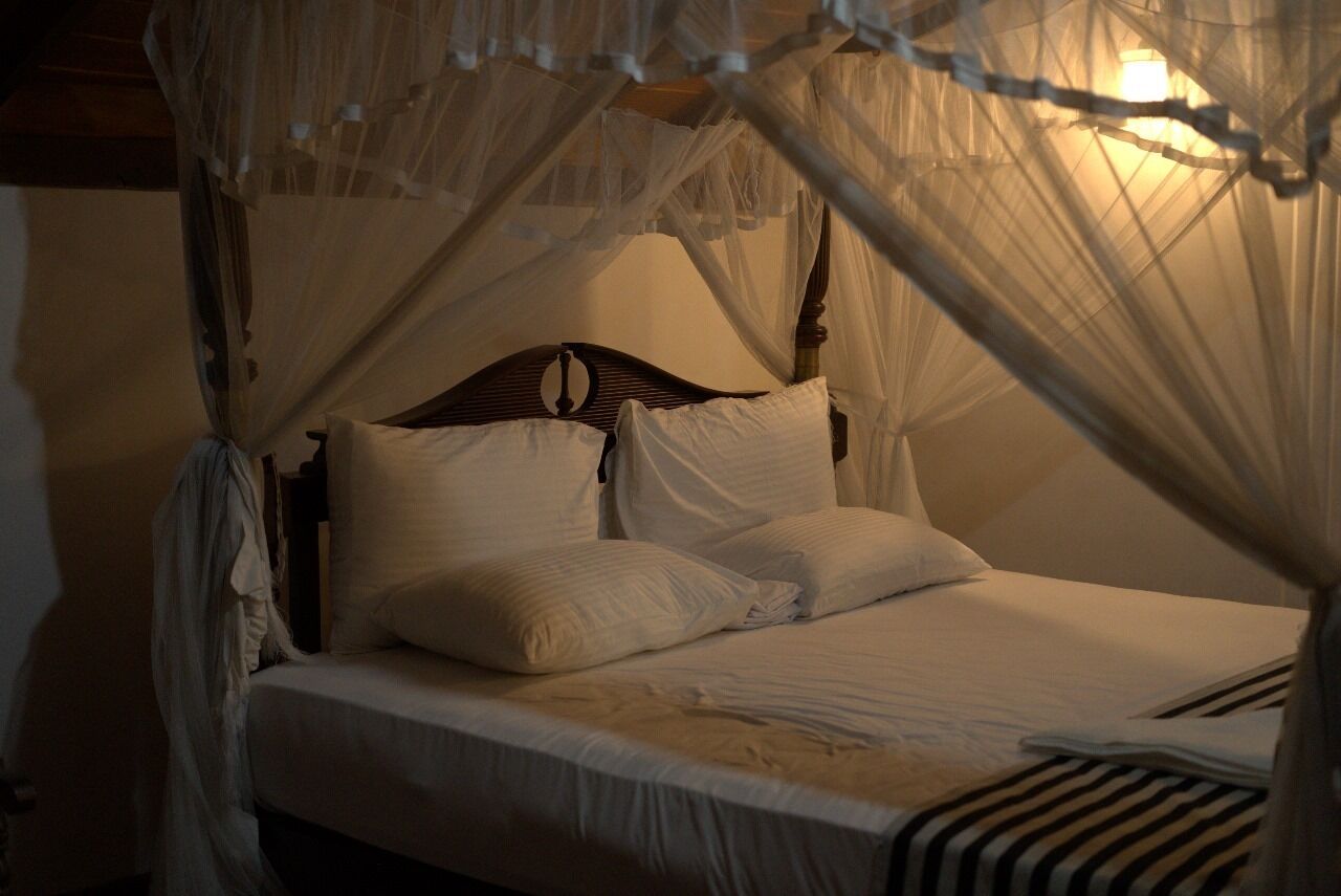Una cama con dosel, ropa de cama blanca y cabecera de madera.