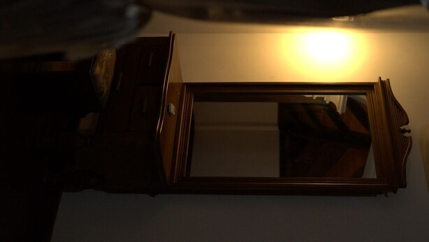 Un miroir avec un cadre en bois, reflétant une pièce dans laquelle se trouve une source de lumière située au-dessus.