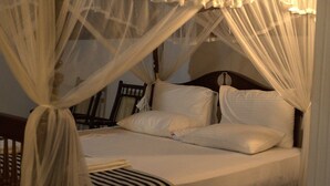 Een bed met witte lakens en een gestreept plaid, een houten hoofdbord, en een stoel op de achtergrond.