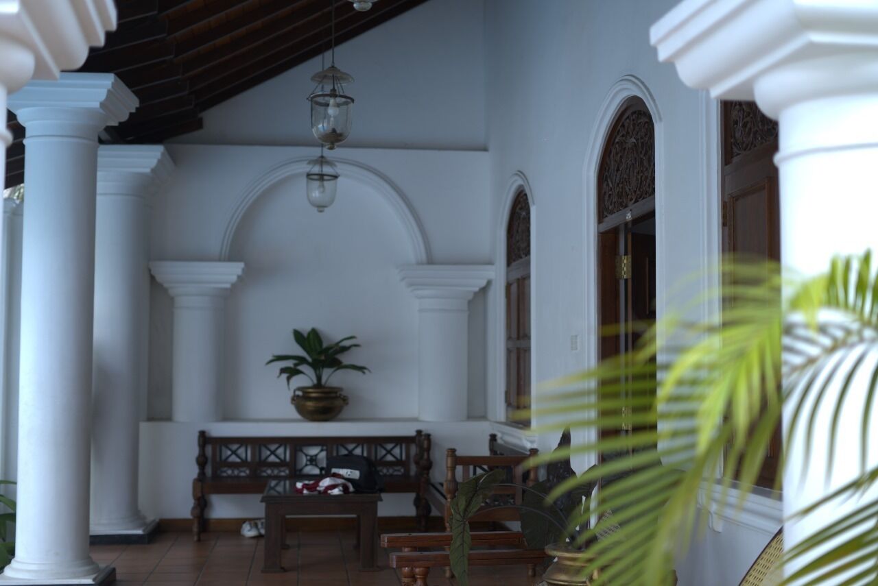 Un porche cubierto con columnas blancas, un banco de madera y faroles colgantes.