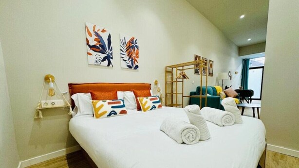 Habitació d'hotel amb un llit gran, un terra de fusta, una tauleta de nit amb una làmpada i dues obres d'art penjades a la paret.