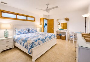 A bedroom with a bed, bedside tables, a desk, a chair, a ceiling fan, and a window.
