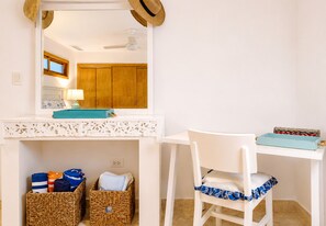 A room with a white desk, a chair, a mirror, a ceiling fan, and two wicker baskets.