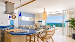 Een moderne keuken met een blauw kookeiland, een eethoek met uitzicht op de oceaan en een gezellige zithoek met een schommelstoel.
