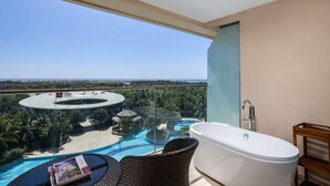 A balcony with a view of a resort pool and a circular building, a white bathtub, and a wicker chair. - Qionghai Bozha Baiyuewan Zhenru Hotel (Qionghai)