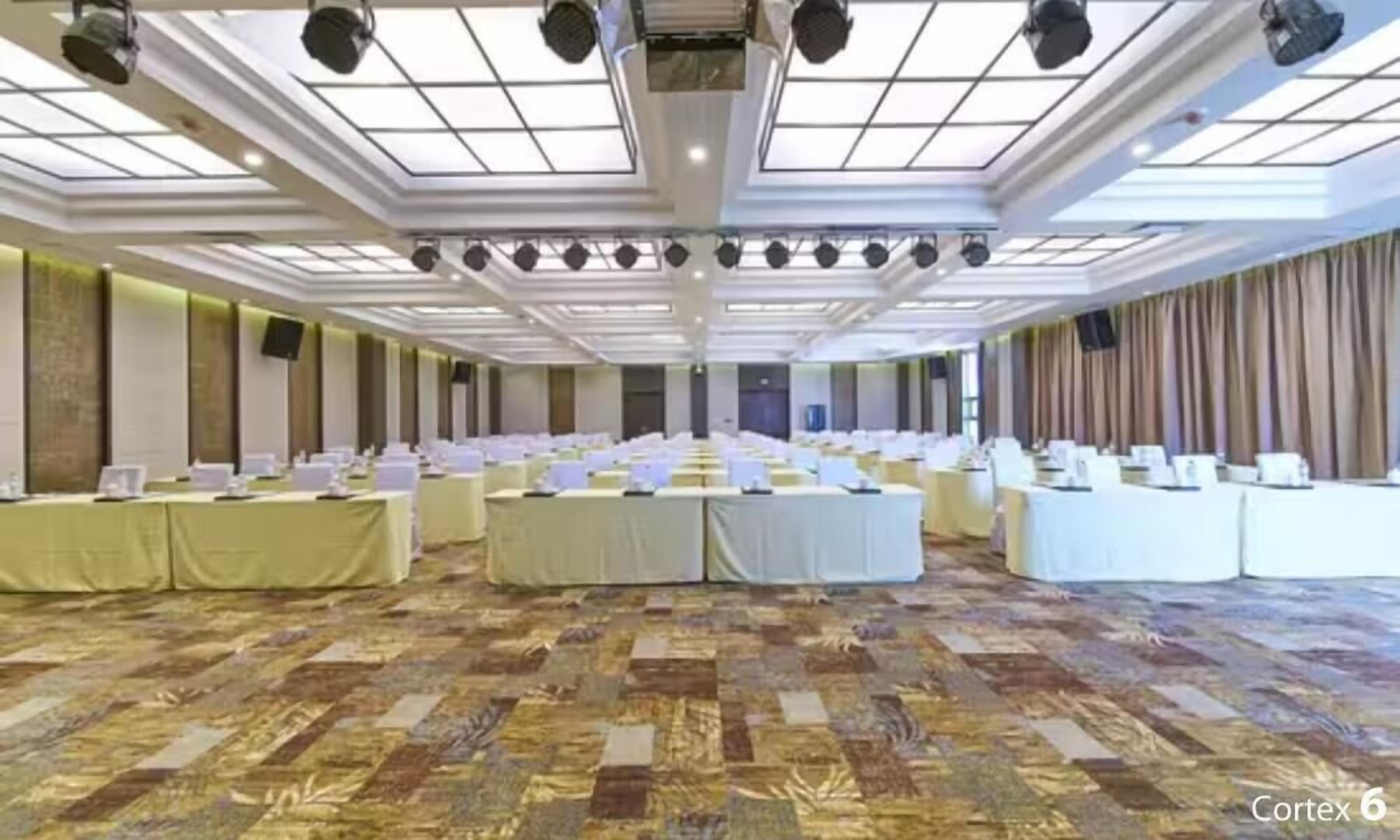 A conference room with multiple tables and chairs, a patterned carpet, and a high ceiling with skylights.